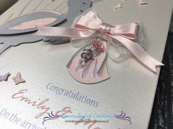 picture of a new baby card, featuring a pink bow , crystal heart & bead charm