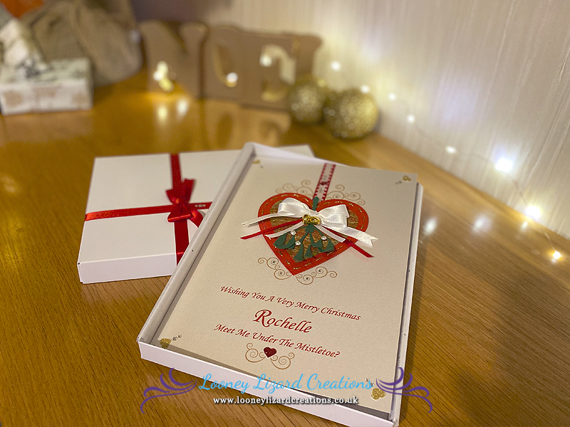 picture of a card featuring a hanging red and gold heart with mistletoe