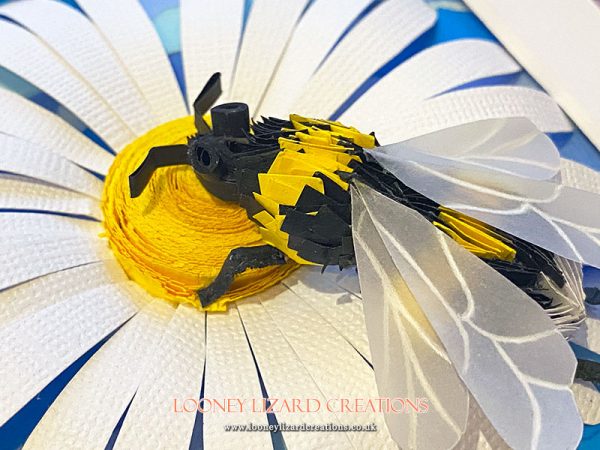 Paper bee sitting on a white daisy with blue background