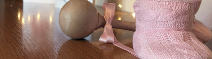 pink baby booties with wooden baby rattle